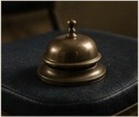 A brass desk bell resting on a black folding chair.